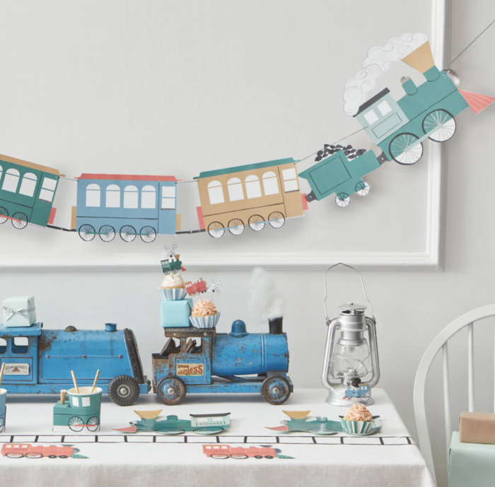 Train garland hanging on the wall with a table with train decorations on it. 