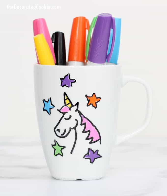 Mug with pens in it and a unicorn design on it. 