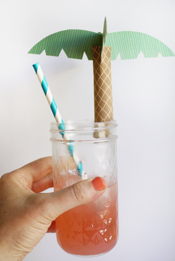 Hand holding a glass that is topped with a paper palm topper. 