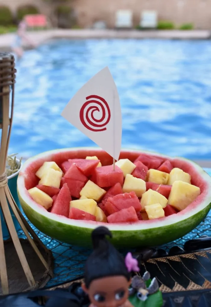 Watermelon boat filled with watermelon and pineapple topped with a small boat sail. 
