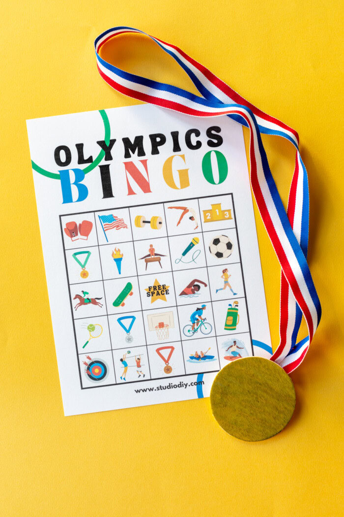 Olympics bingo pdf on a yellow background next to a gold medal. 