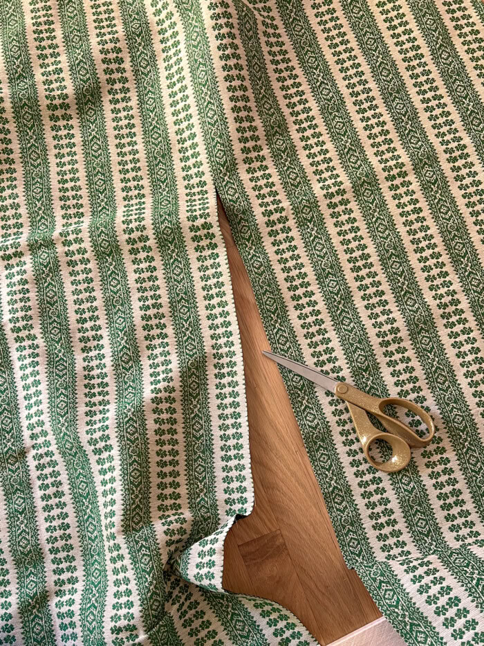 Green striped floral fabric being cut with gold scissors