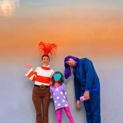 Family wearing Inside Out 2 costumes in front of ombre wall